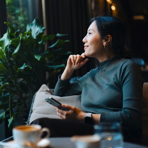 Kvinne sitter med mobil og kaffekopp. 
