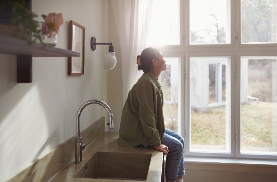 En kvinne sitter på en kjøkkenbenk og ser ut av vinduet. Foto.
